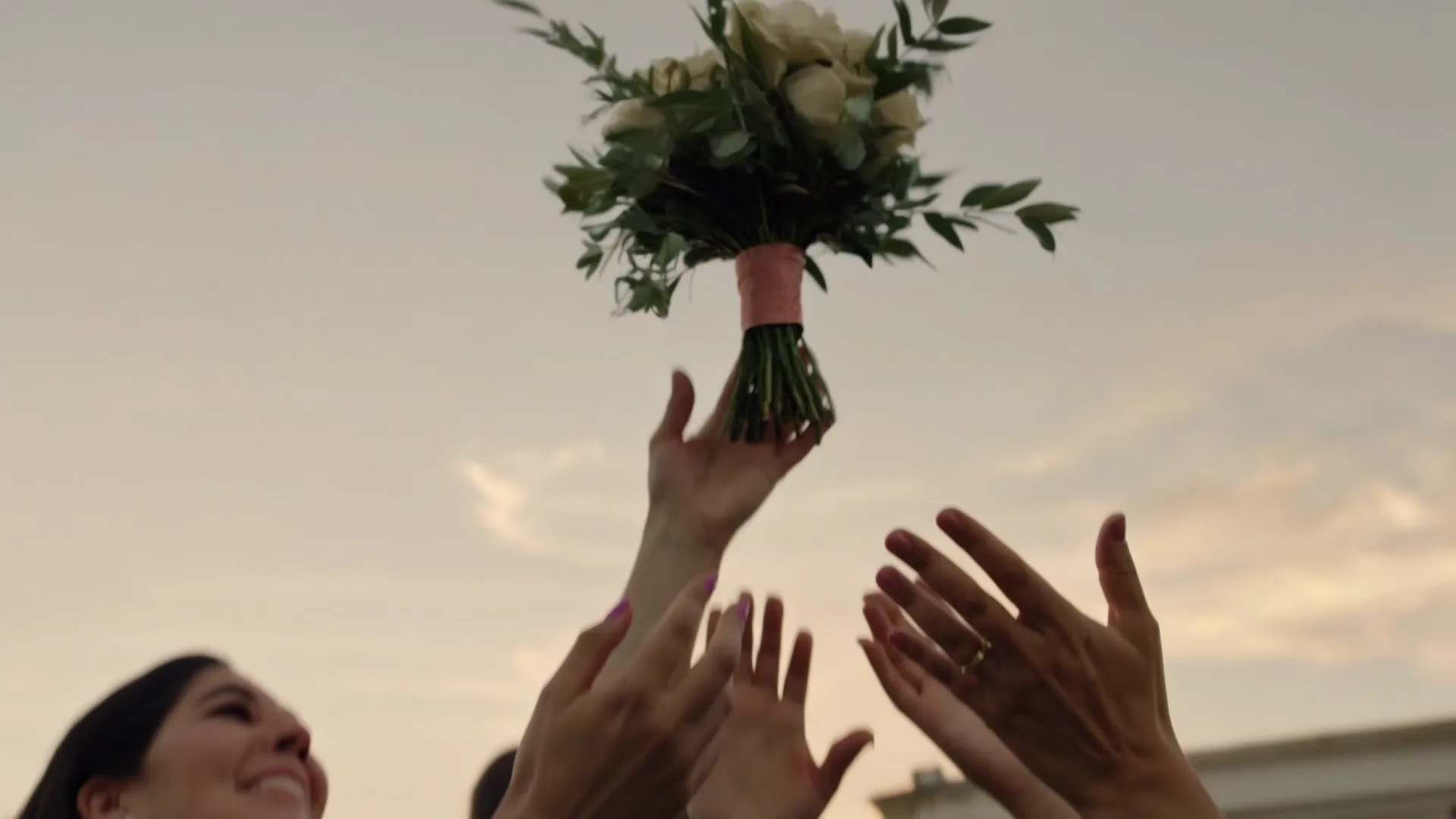 A bridal bouquet released into the evening sky above a pair of outstretched hands.